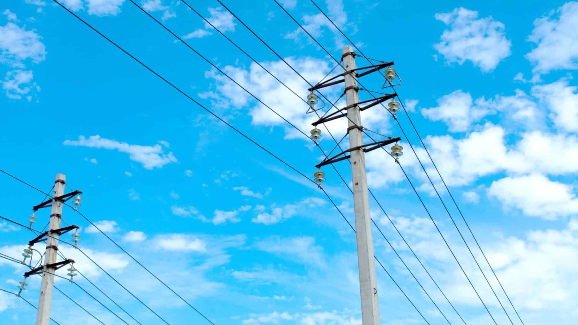 Power lines against a cloudy blue sky, supporting smart power distribution with grid modernization and reliable delivery.